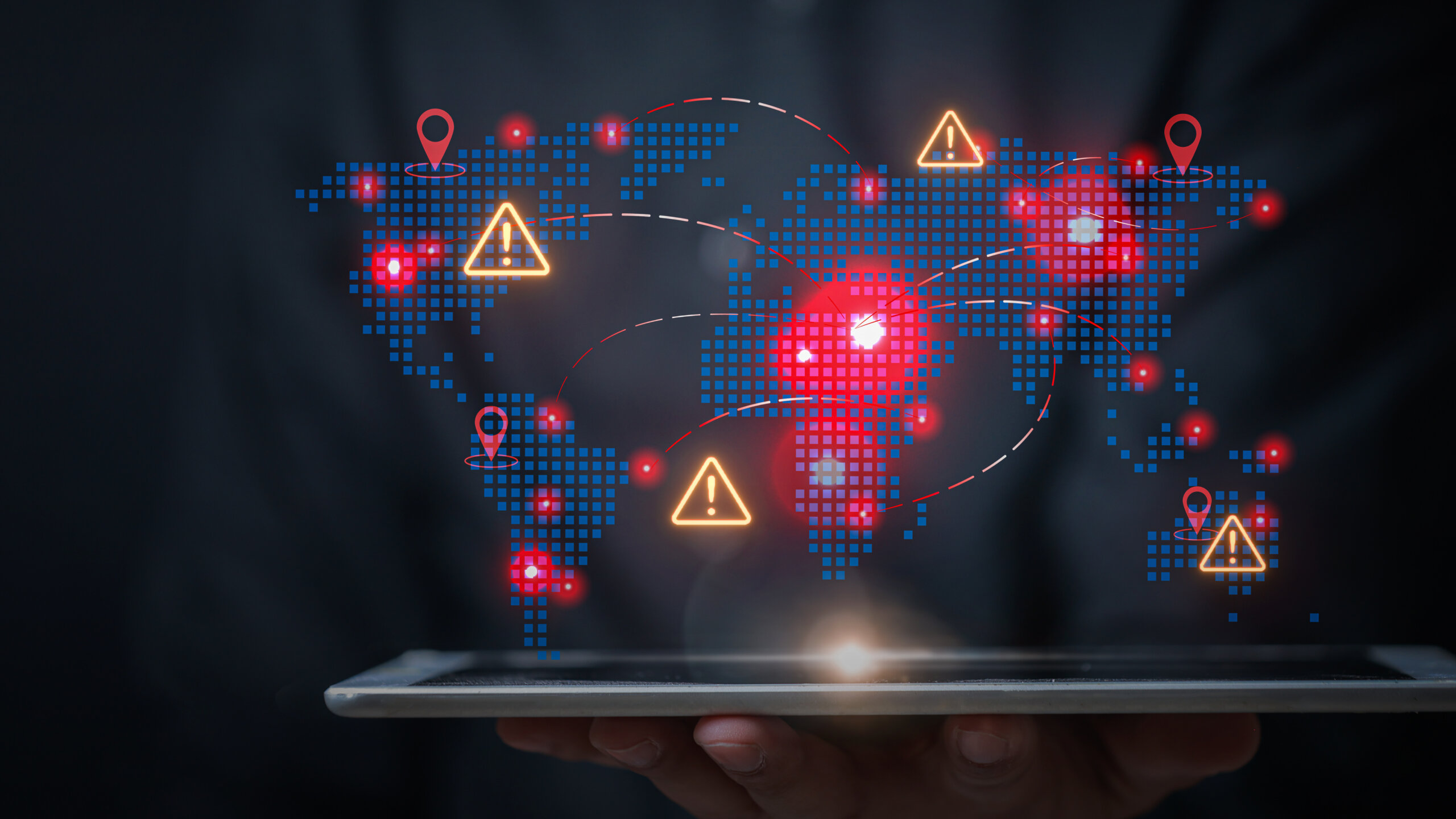 Serious businessman holding tablet showing global distribution network map with warning sign highlighting danger and urgent risk level